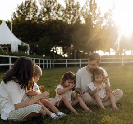 Family sitting on grass enjoying leisure time outdoors, with sun setting in the background.
