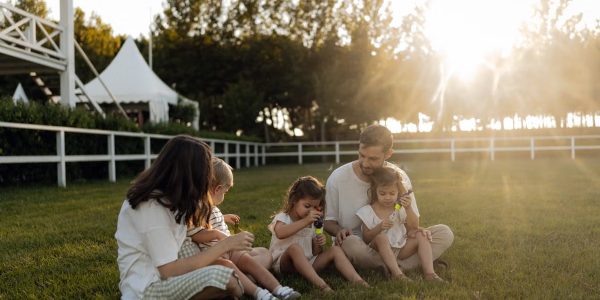 Family sitting on grass enjoying leisure time outdoors, with sun setting in the background.