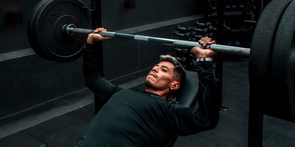 Man performing bench press with heavy barbell in a gym setting, focusing on strength training.